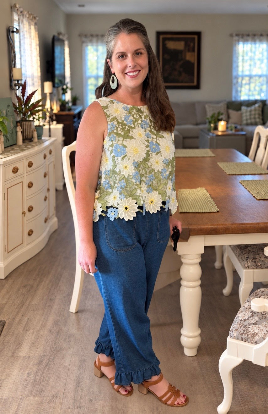 Jenny Frickie smiling in a floral lace top, ruffle-hem jeans, statement earrings, and brown sandals.
