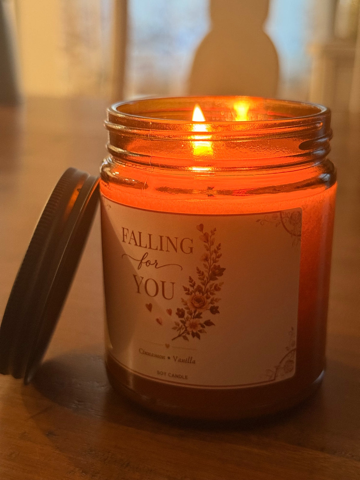Actual Falling for You cinnamon vanilla candle burning in its amber jar on a wooden table.