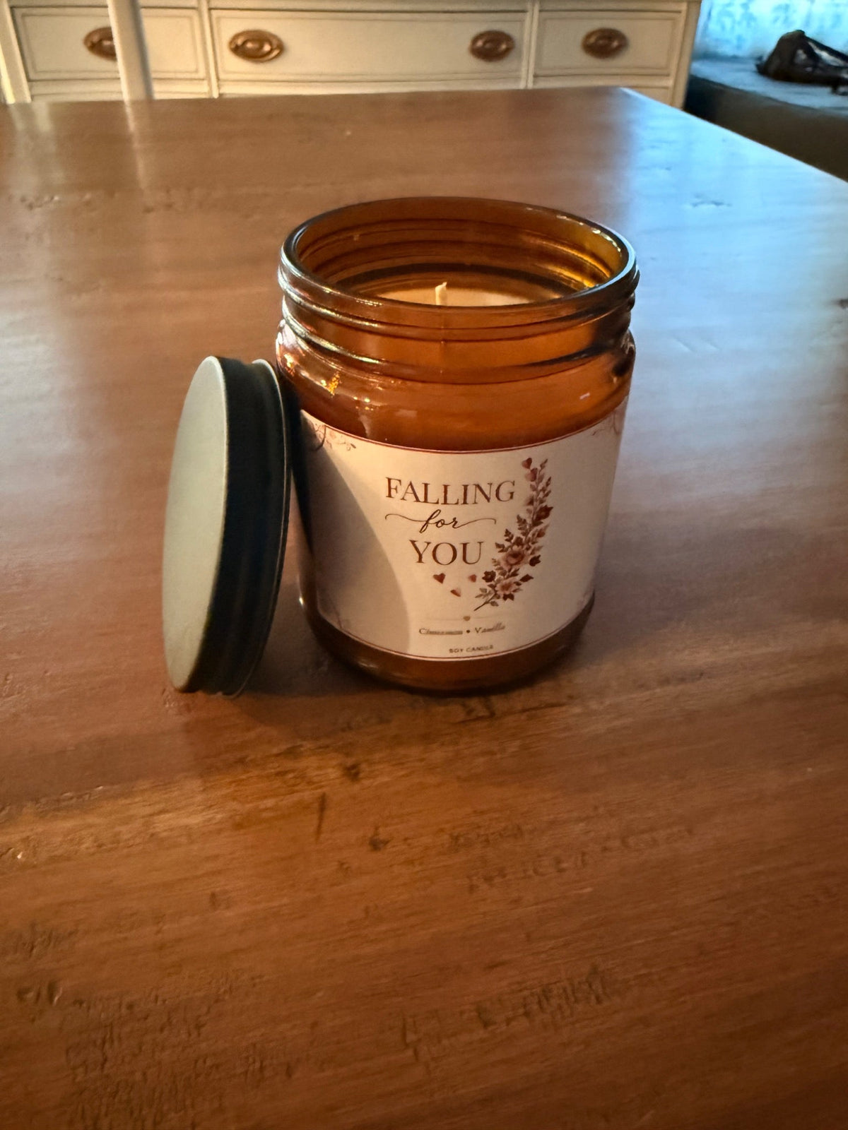 Actual unlit Falling for You candle with floral label and black lid on a wooden table.