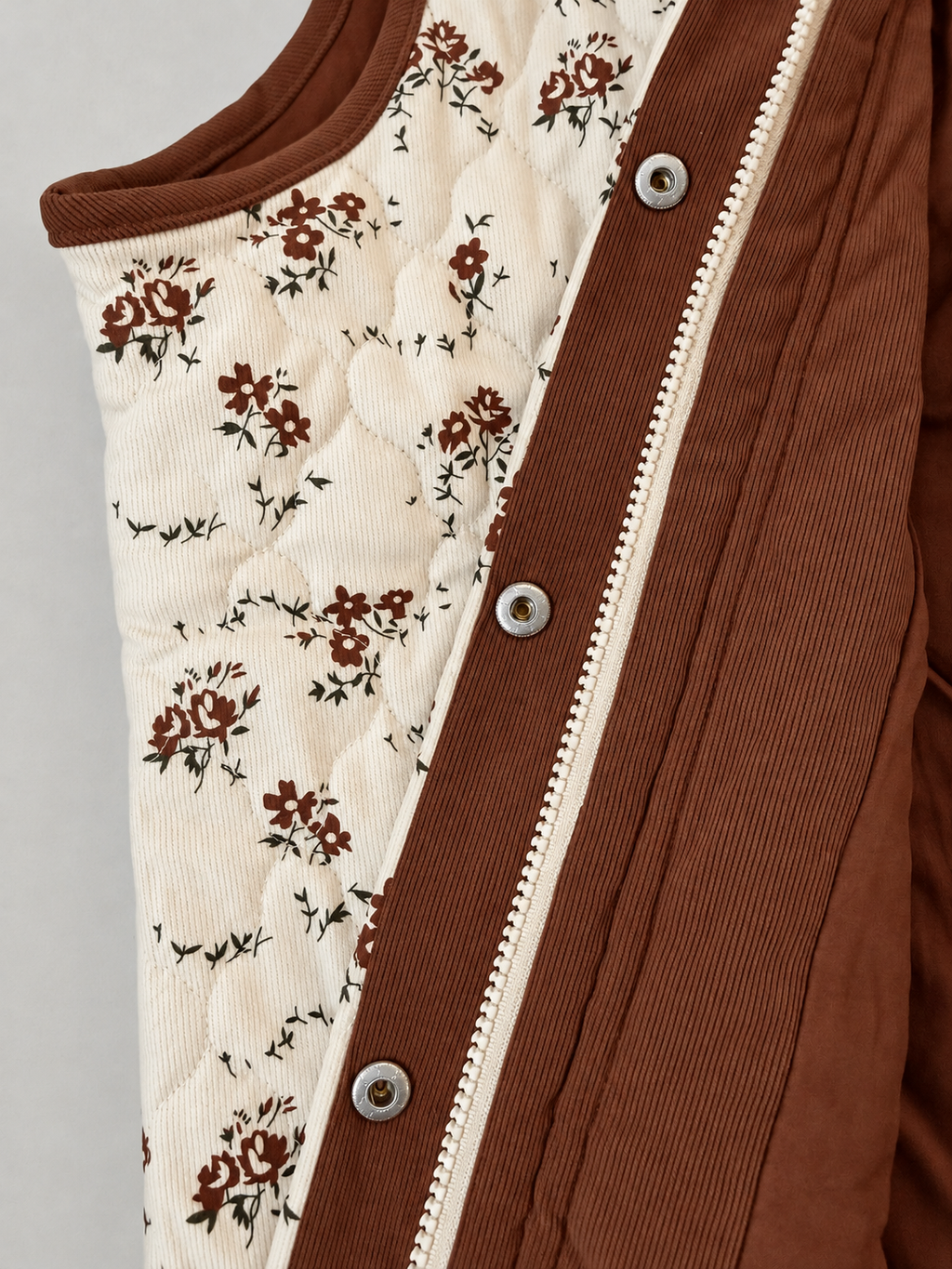 Close-up of the Meadow Bloom Quilted Zip Vest showing ribbed floral fabric, curved quilting, brown facing, zipper and silver snaps.