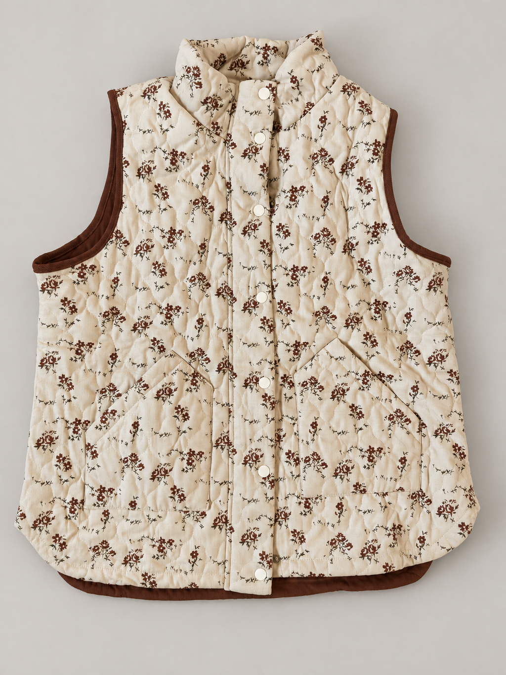 Meadow Bloom Quilted Zip Vest laid flat with the snap front closed, showing cream floral fabric, brown trim and two patch pockets.