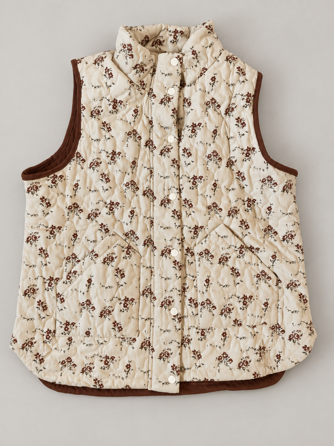 Meadow Bloom Quilted Zip Vest laid flat with the snap front closed, showing cream floral fabric, brown trim and two patch pockets.